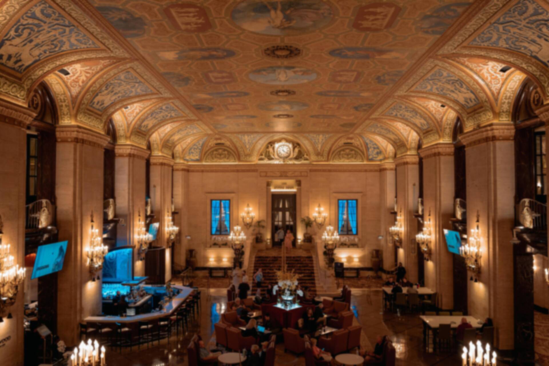 Wide shot of a grand luxurious hotel lobby with a golden dome ceiling, bustling with diverse staff and guests