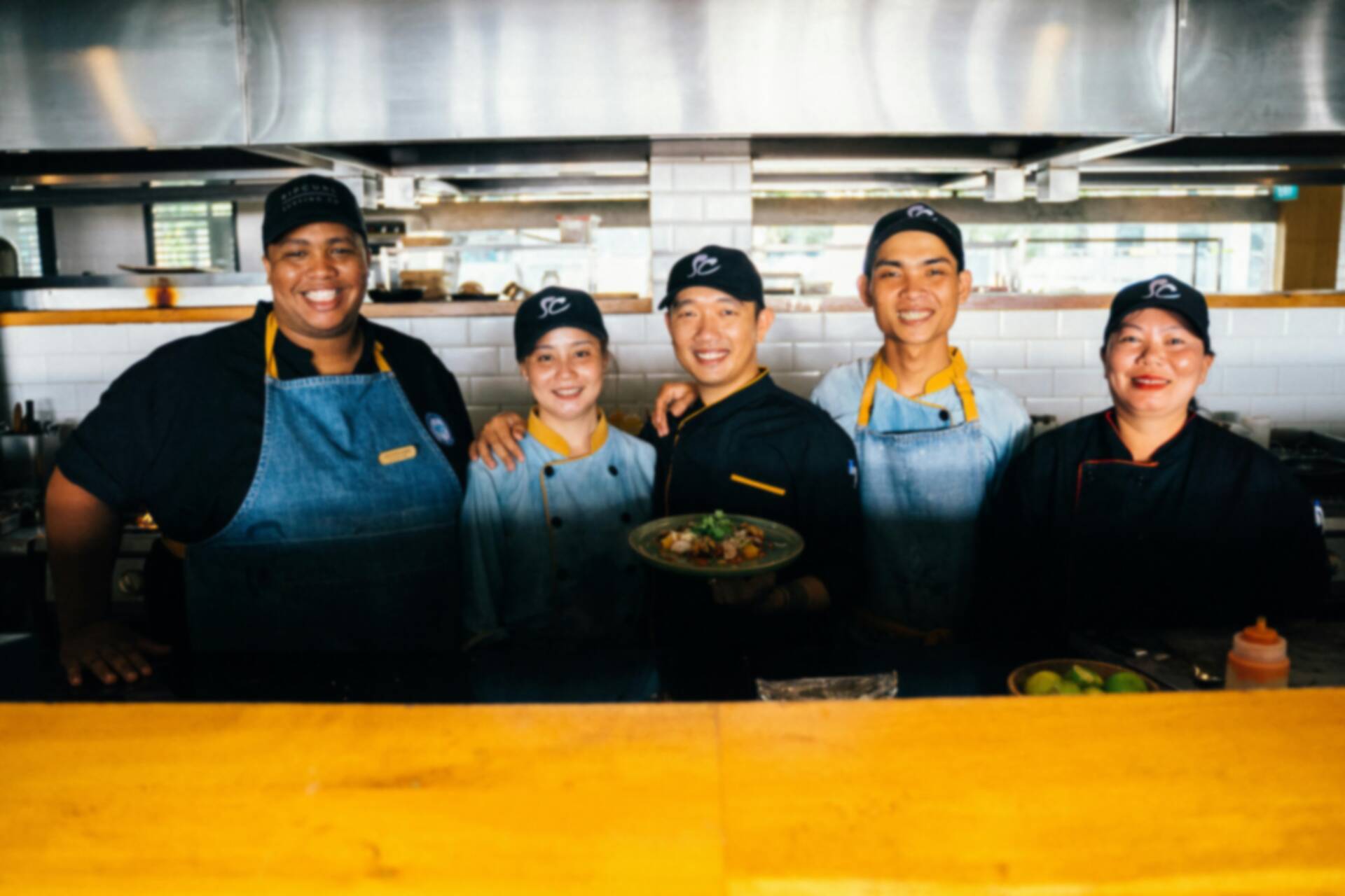 A group portrait of a restaurant staff in a busy kitchen, smiling