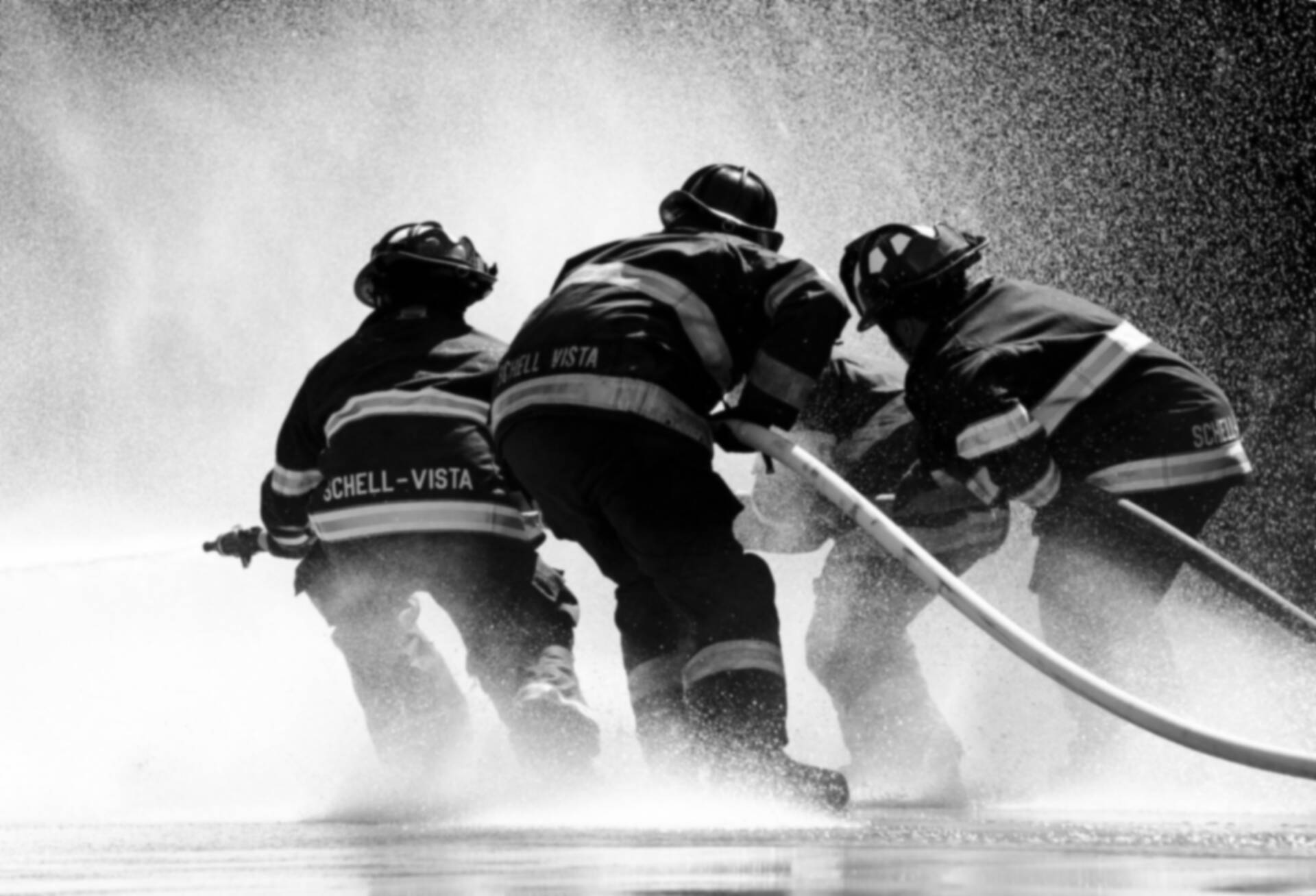 Dramatic shot of a team of firefighters, operating a fire hose together, silhouetted against a backdrop of smoke
