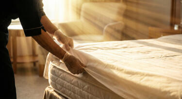 Professional housekeeper tucking fresh linens in a luxury hotel room | EvoKomms